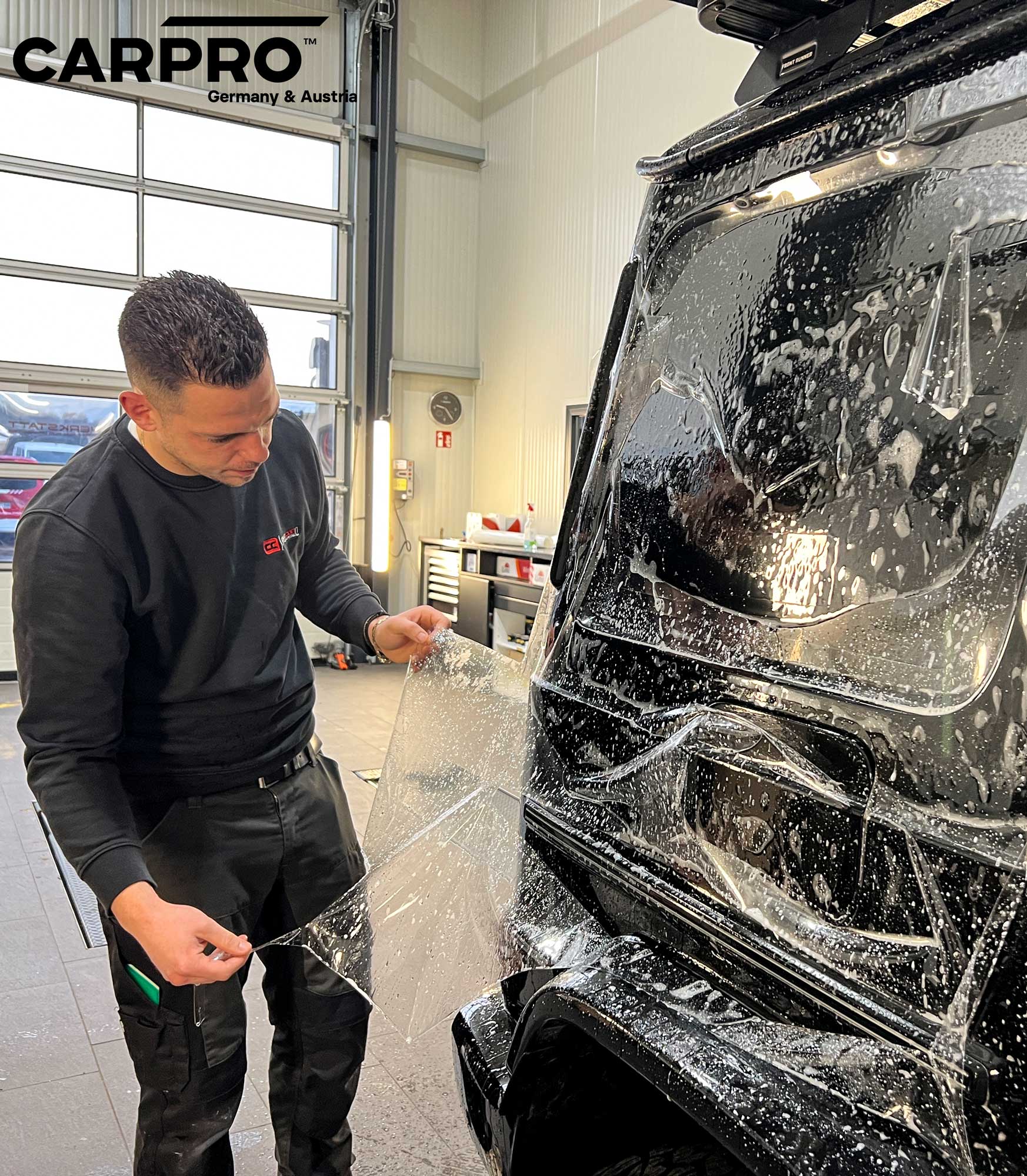 CarCon GmbH Inhaber Chris Mavrikis als Person auf dem Bild. er bringt Paint Protection Film von der Marke CarPro an ein Fahrzeug. Das Bild zeigt auch die Lackschutzfolie nass auf dem Fahrzeug foliert. Das Bild wurde aufgenommen iim CarCon Standort in Verden.