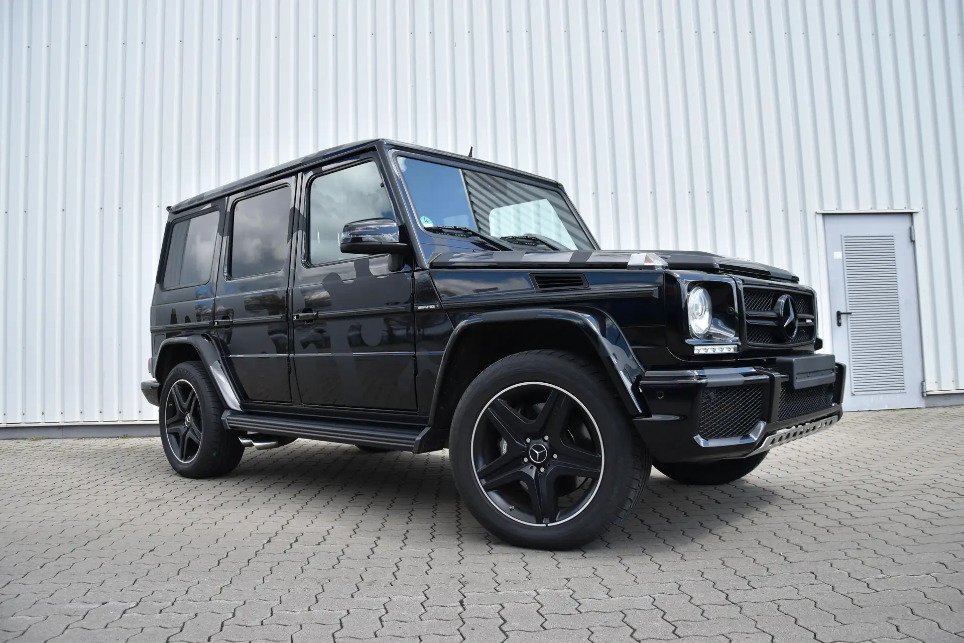 Mercedes Benz G-Klasse foliert mit Military Camouflage Design. Steht vor dem Hallentor. Es sind leichte Tarnflecken in Mattschwarz zu sehen.