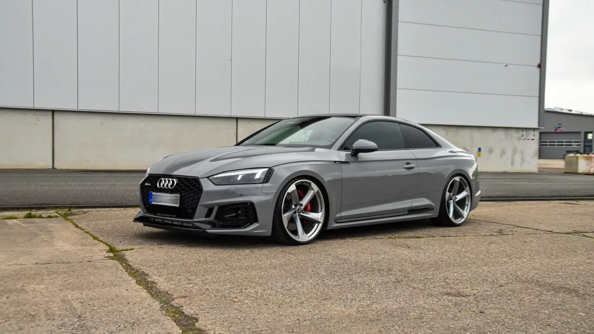 Audi RS4 in Nardogrey foliert wird mit großen Felgen vom Audi RS8 gezeigt. Die Felgen fallen wegen der Größe und individuellen Art auf. Das Fahrzeug steht vor einer Messehalle in Verden.